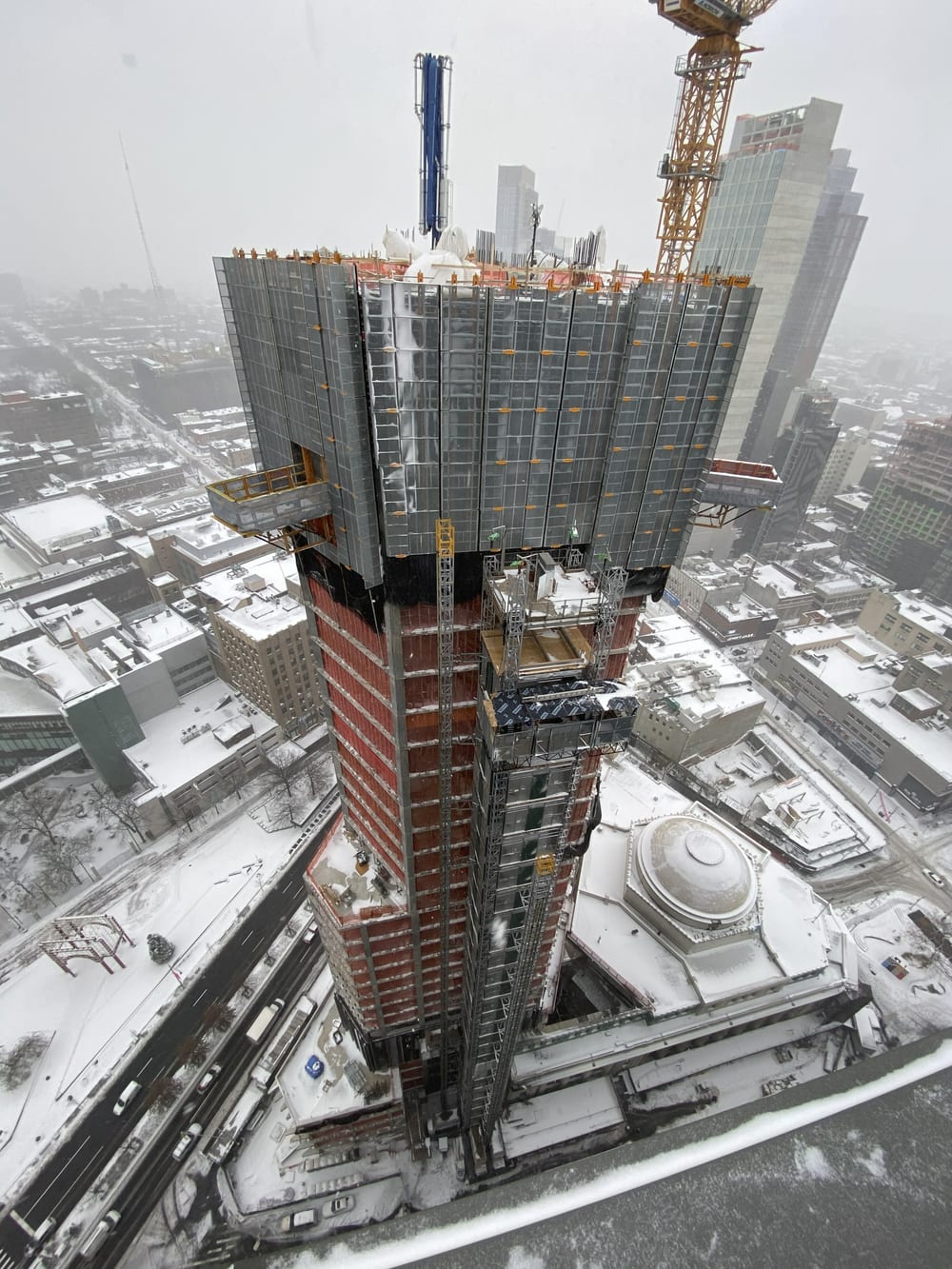 Aerial view down The Brooklyn Tower during winter concrete operations, formwork and beltwall rising above a snow-covered downtown Brooklyn